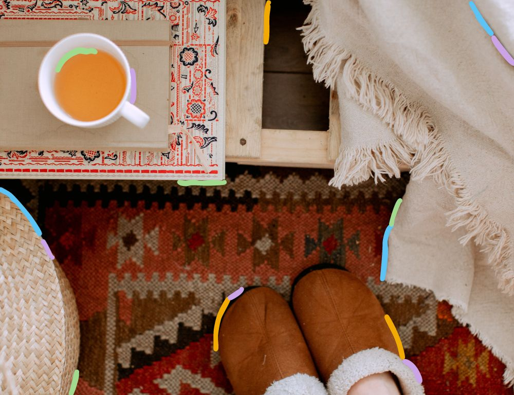 Feet in slippers next to a coffee table with a cup of tea and blankets