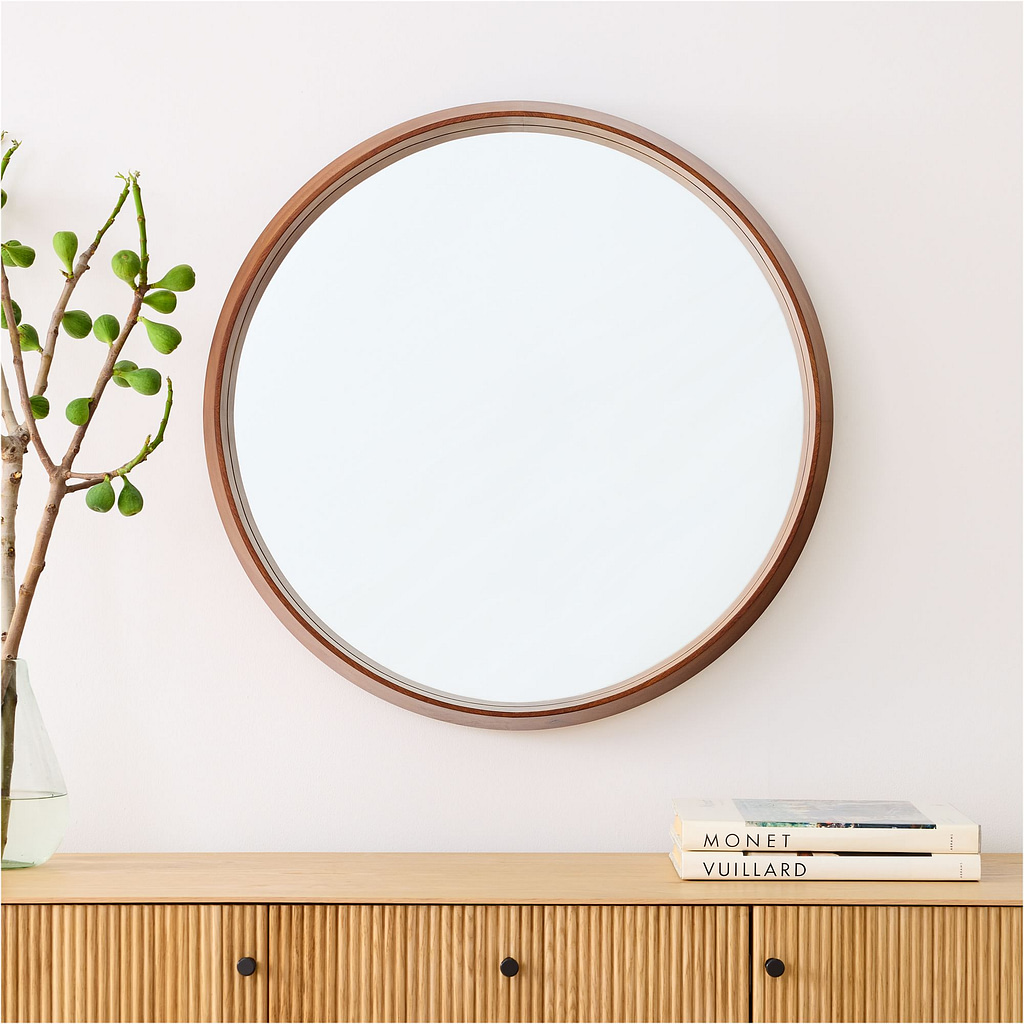 West elm circular mirror with wooden frame hanging above a wooden drawer set